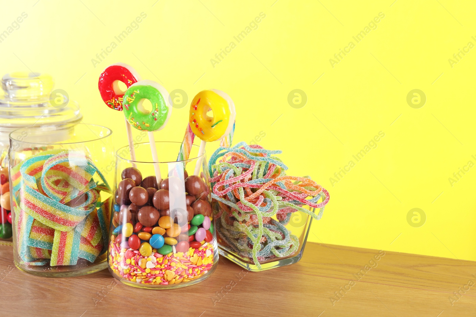 Photo of Candy bar. Many different sweets on wooden table against yellow background. Space for text