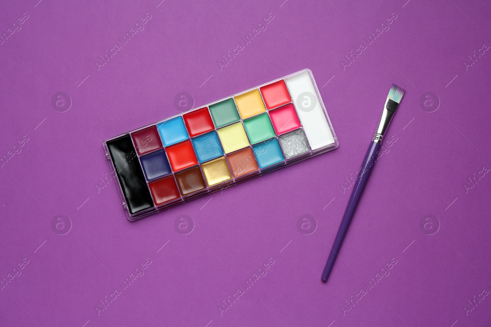 Face paints and brush on purple background, top view Photo of Face paints and brush on purple background, top view