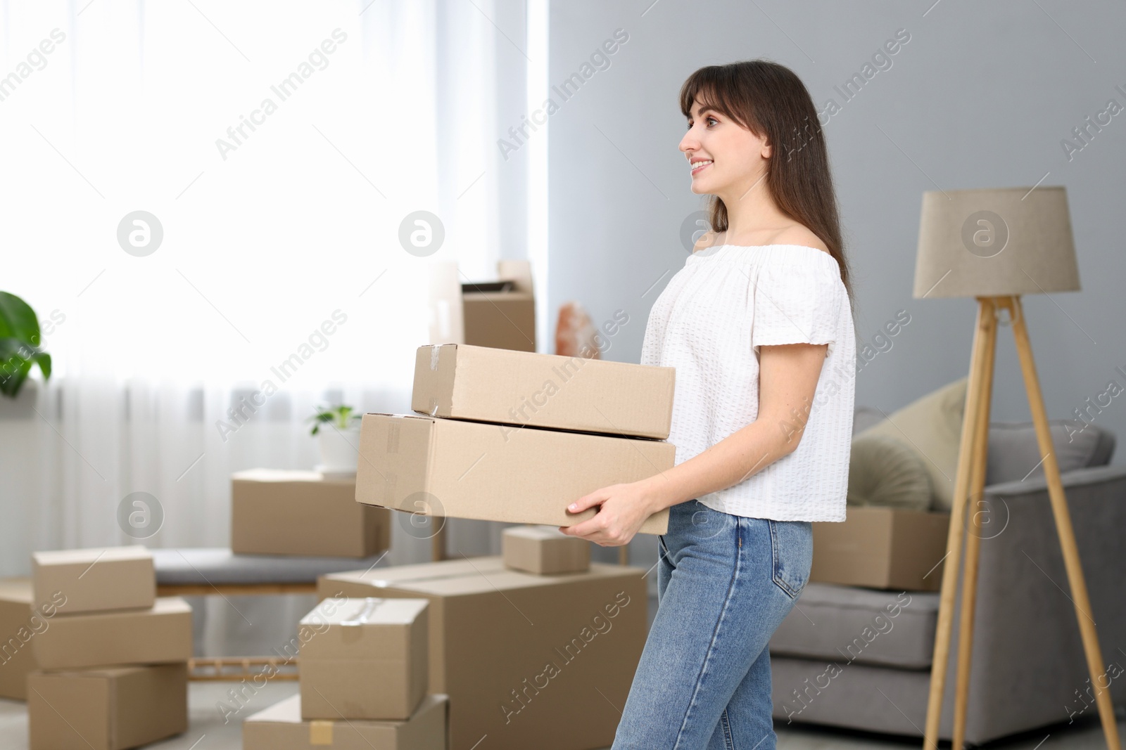 Photo of Moving day. Happy woman with cardboard boxes in her new home