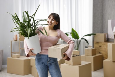 Moving day. Happy woman with cardboard box and houseplant in her new home