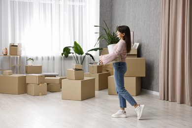 Photo of Moving day. Happy woman with cardboard box and houseplant in her new home