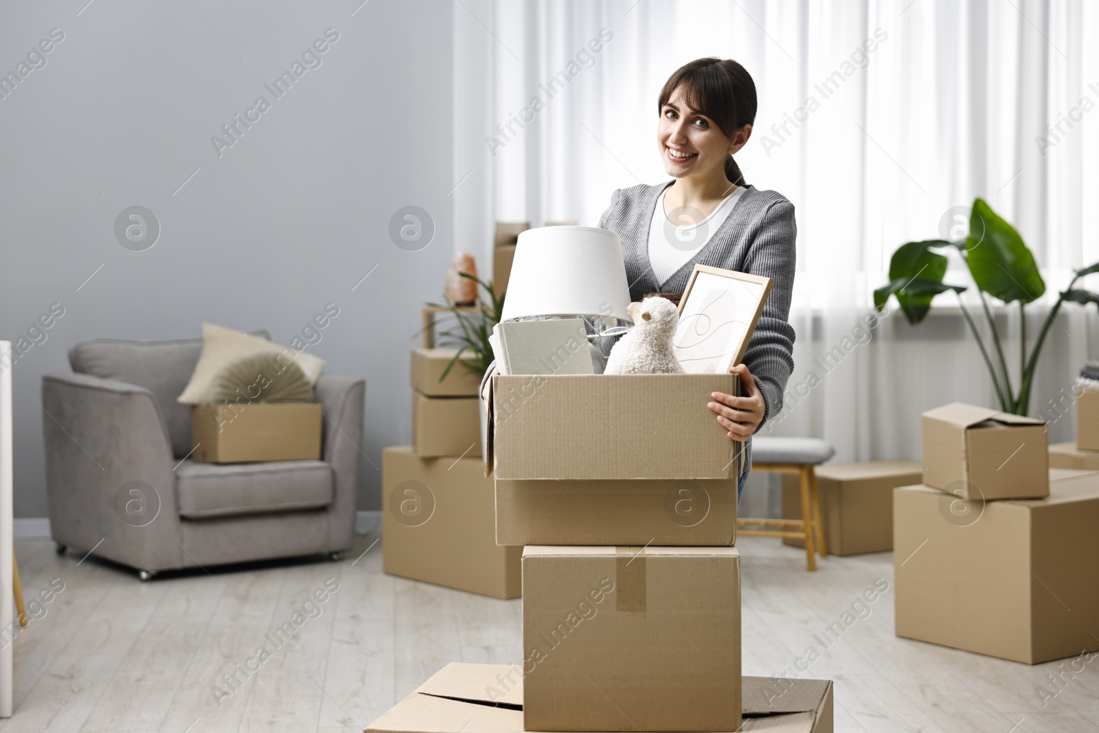 Photo of Moving day. Happy woman with her belongings in new home, space for text