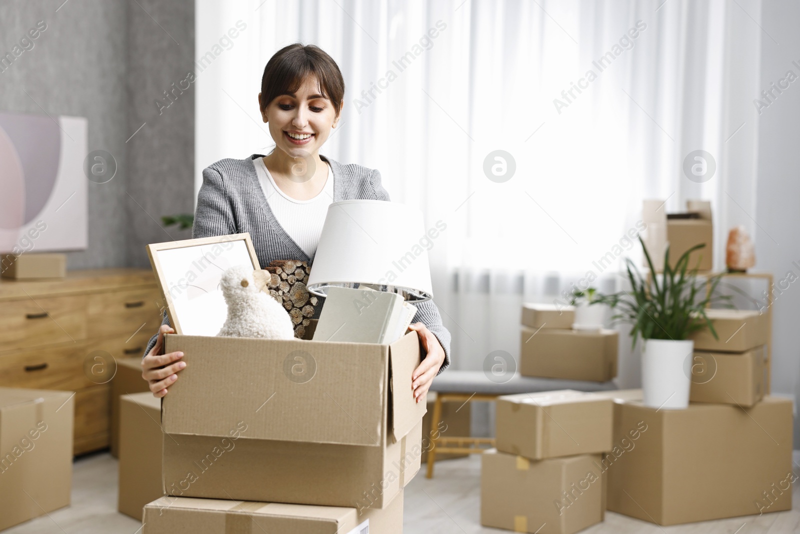 Photo of Moving day. Happy woman with her belongings in new home, space for text