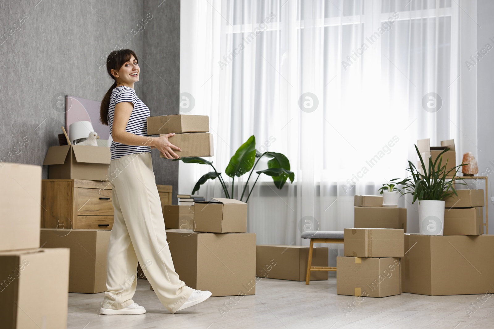 Photo of Moving day. Happy woman with cardboard boxes in her new home