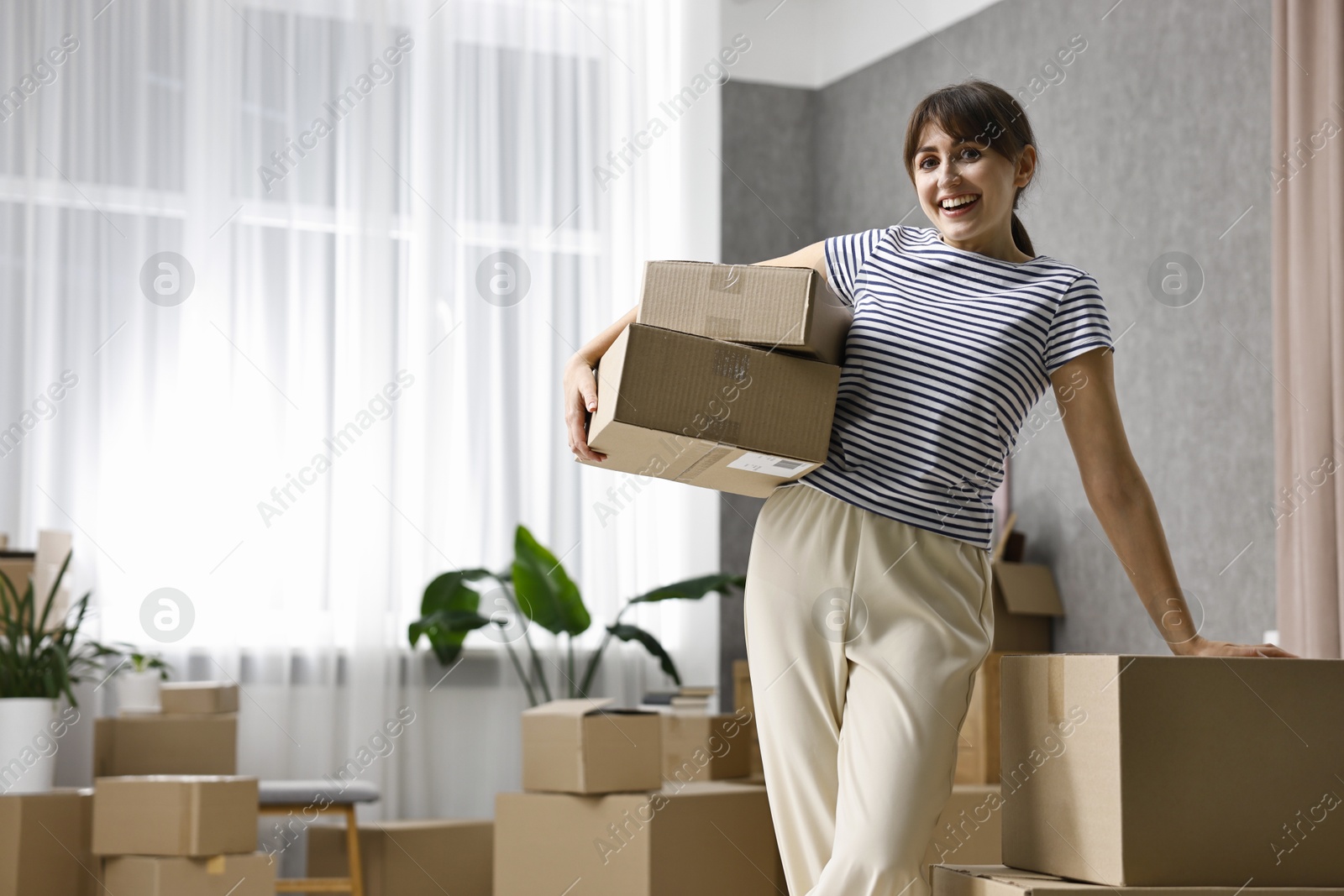 Photo of Moving day. Happy woman with cardboard boxes in her new home, space for text