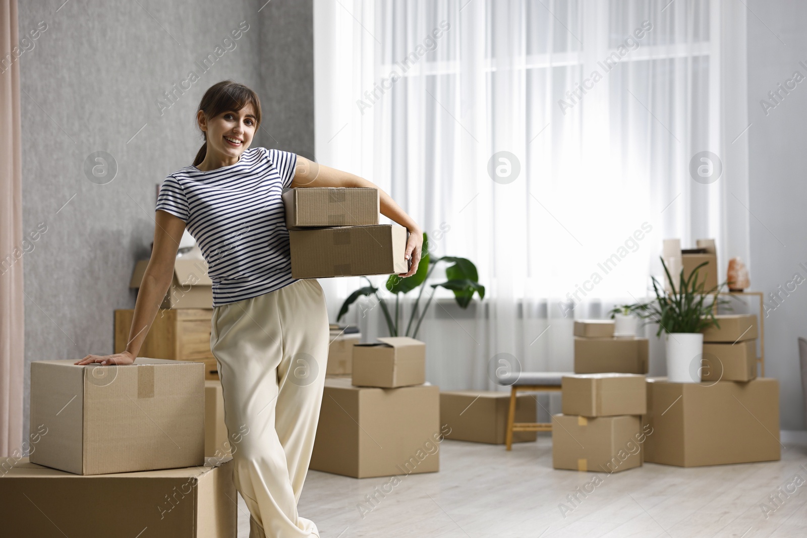 Photo of Moving day. Happy woman with cardboard boxes in her new home, space for text