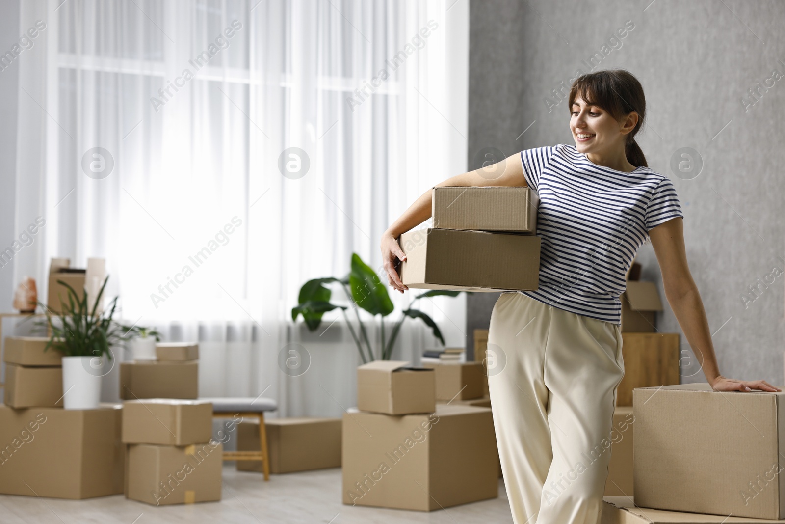 Photo of Moving day. Happy woman with cardboard boxes in her new home, space for text