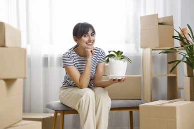 Moving day. Happy woman with houseplant and cardboard boxes in her new home