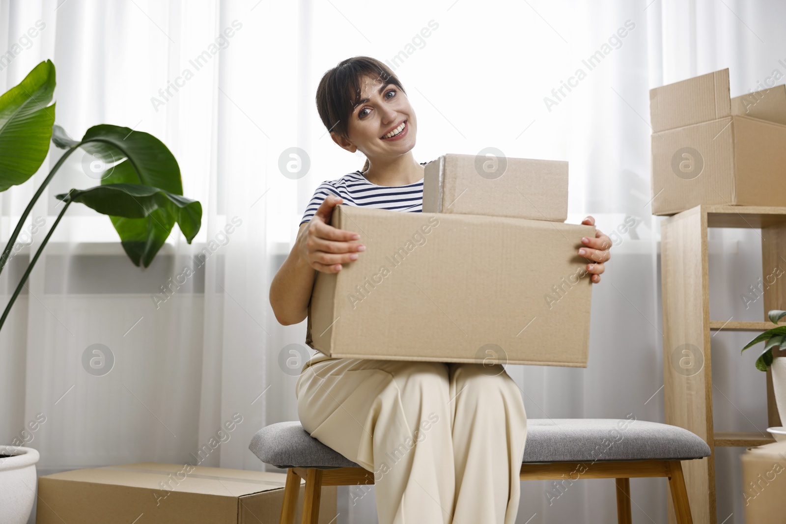 Photo of Moving day. Happy woman with cardboard boxes in her new home