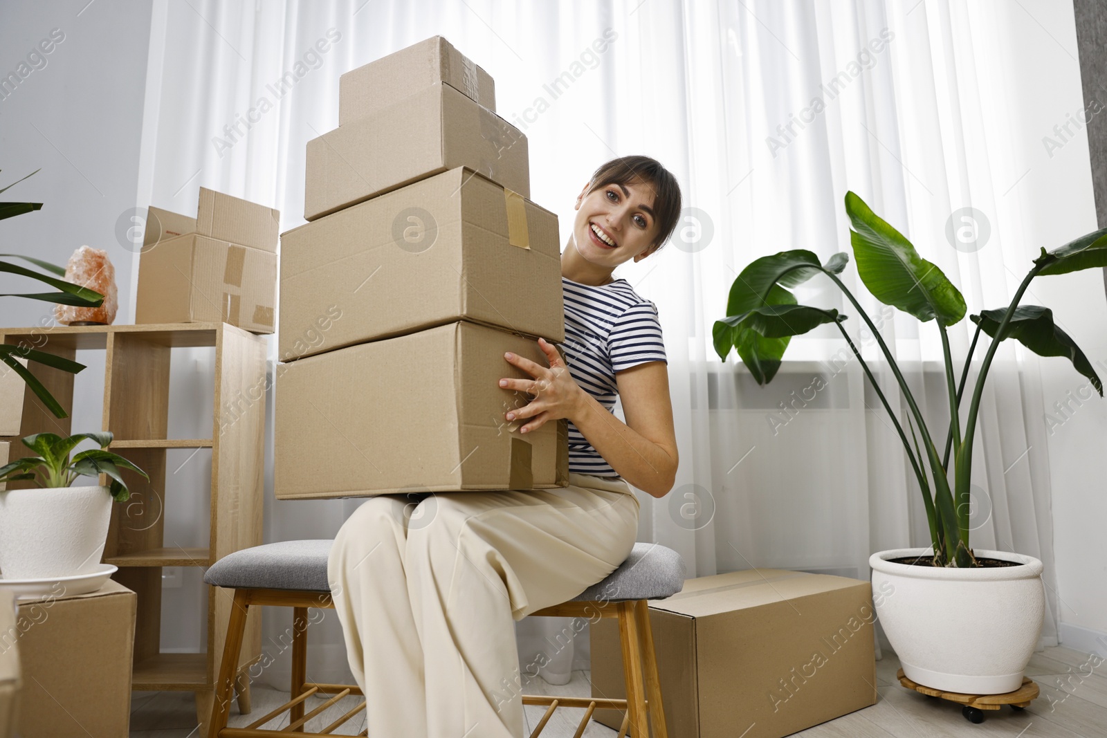 Photo of Moving day. Happy woman with cardboard boxes in her new home