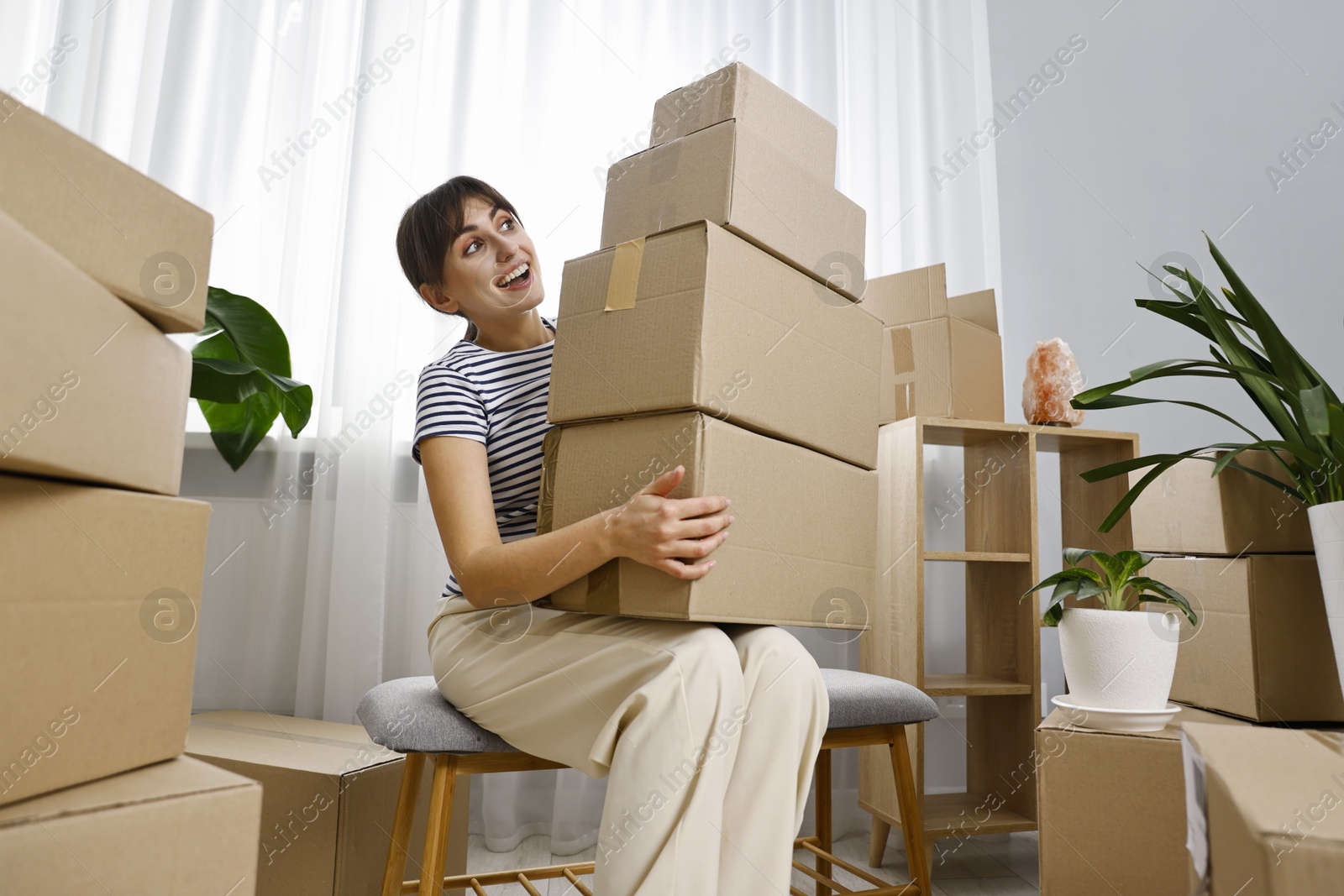 Photo of Moving day. Happy woman with cardboard boxes in her new home