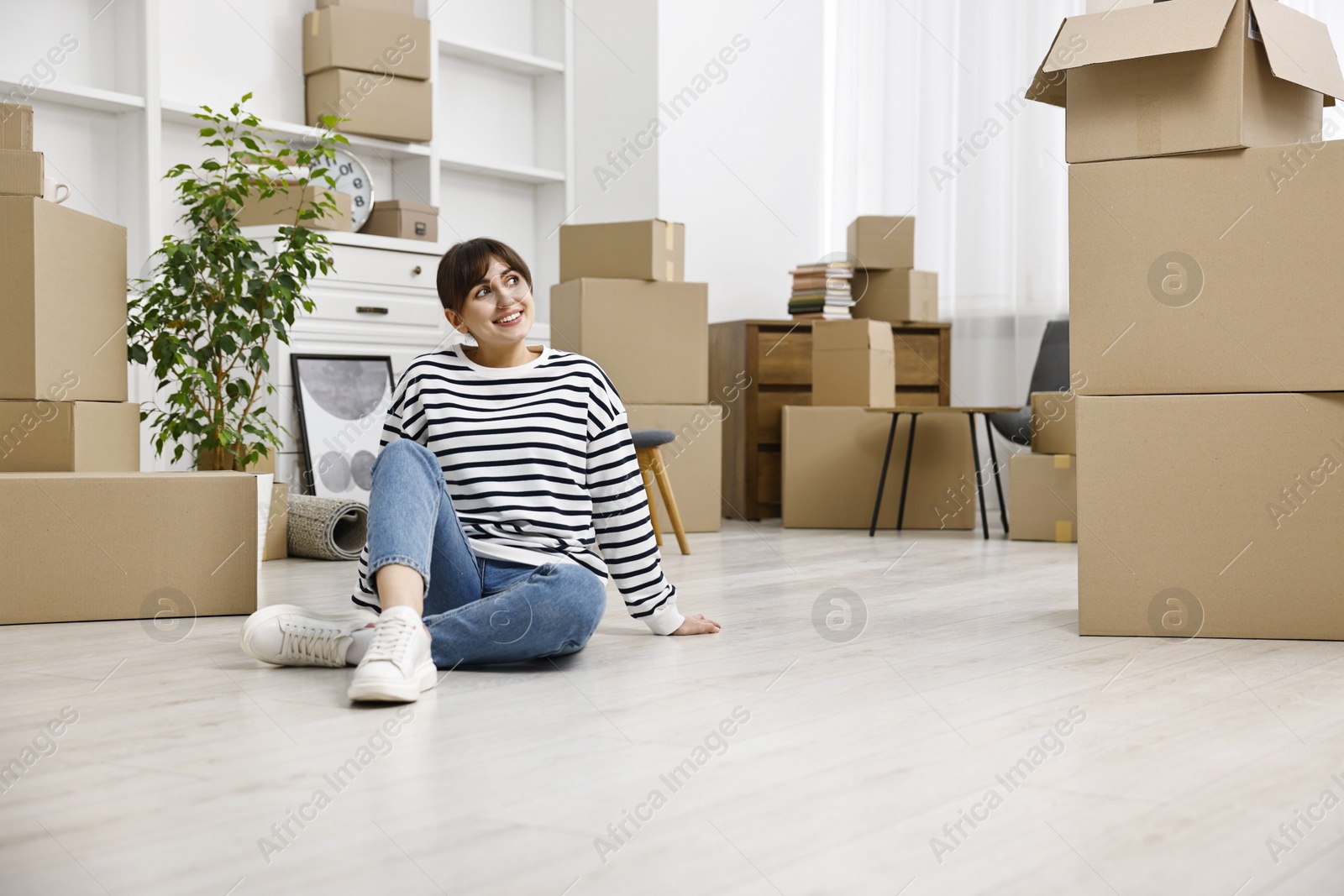 Photo of Moving day. Happy woman resting on floor and cardboard boxes in her new home