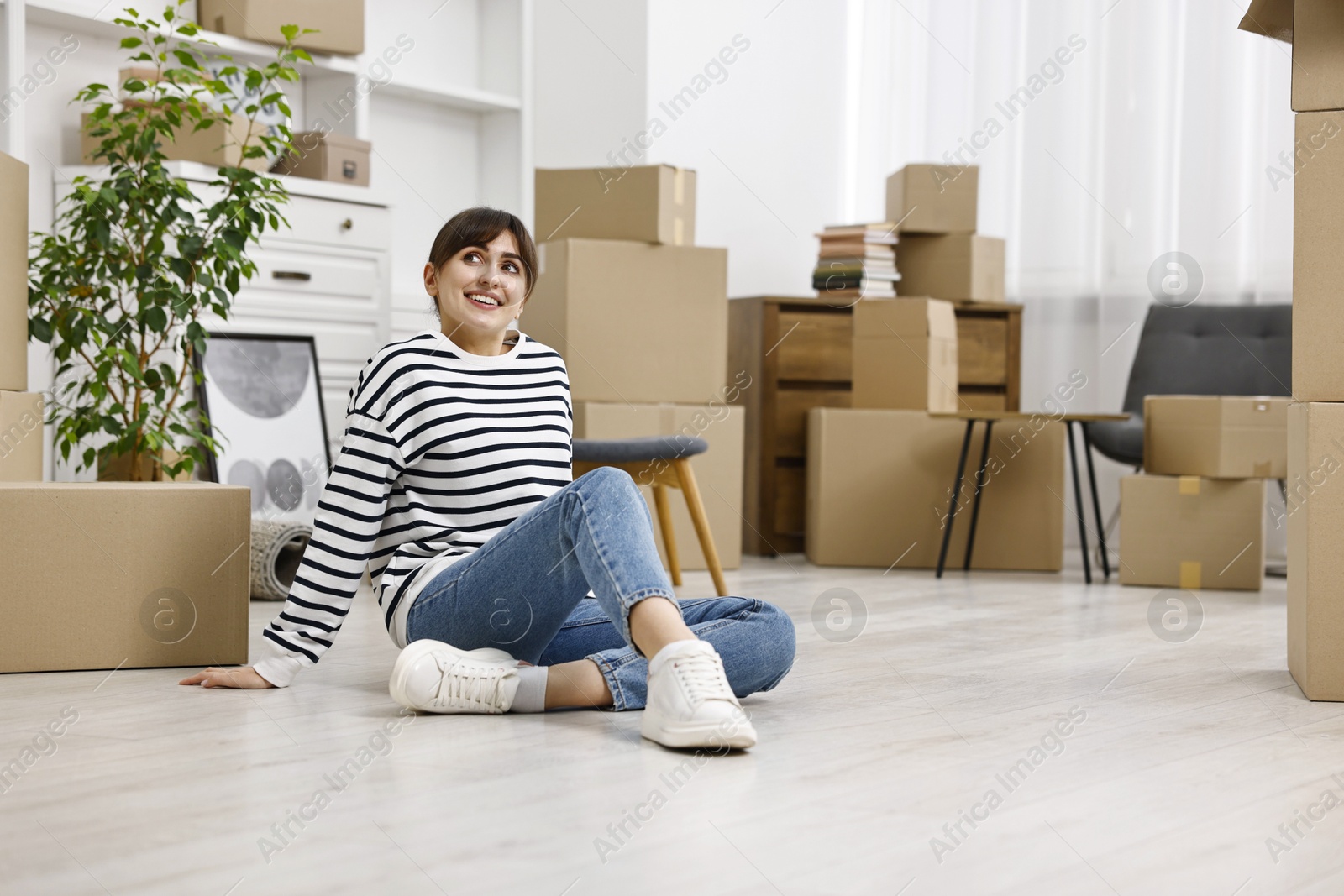 Photo of Moving day. Happy woman resting on floor and cardboard boxes in her new home