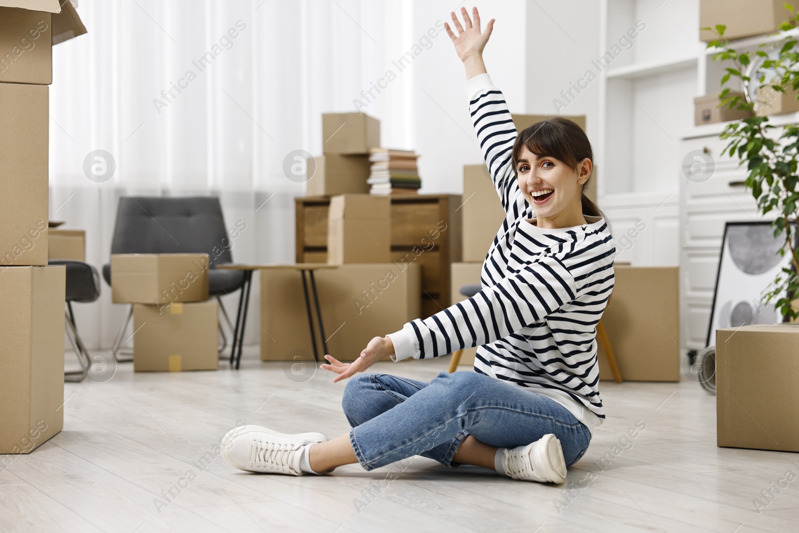 Photo of Moving day. Happy woman resting on floor and cardboard boxes in her new home