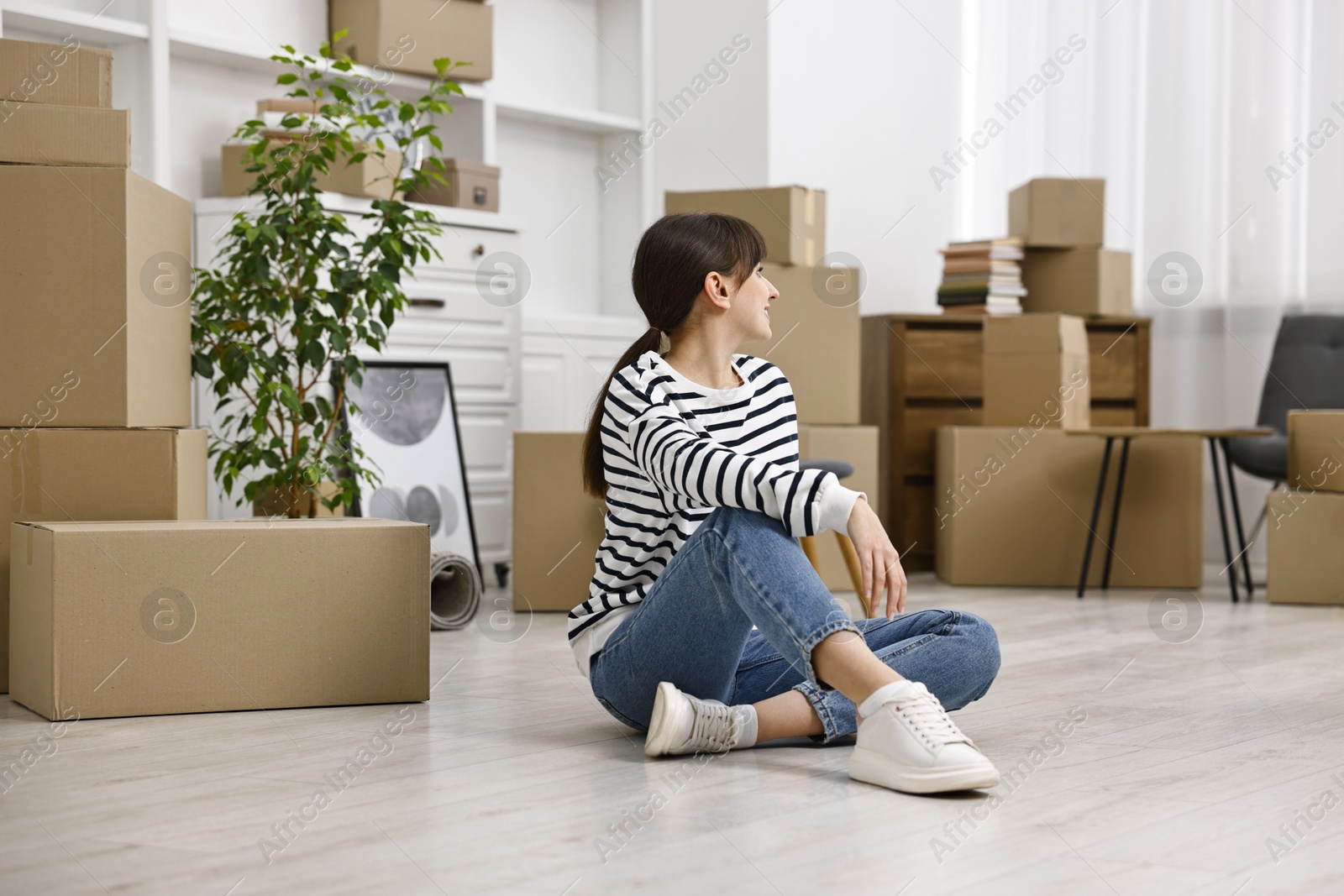 Photo of Moving day. Happy woman resting on floor and cardboard boxes in her new home