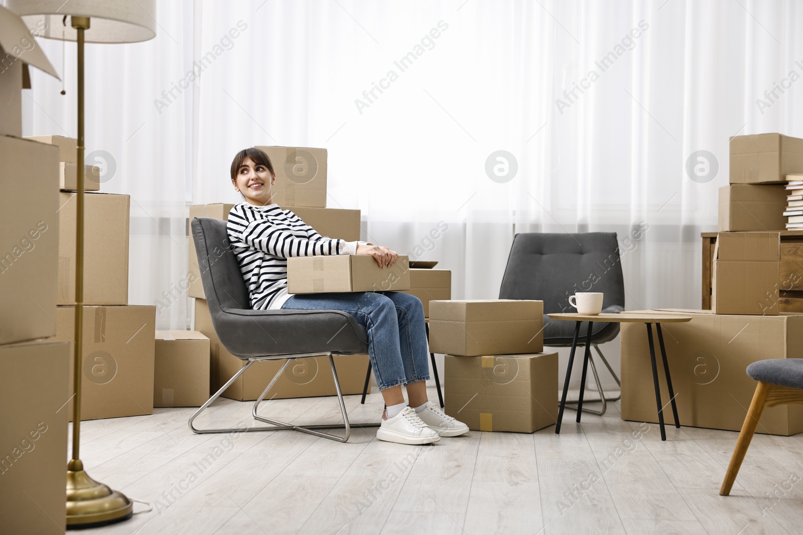 Photo of Moving day. Happy woman with cardboard box in her new home