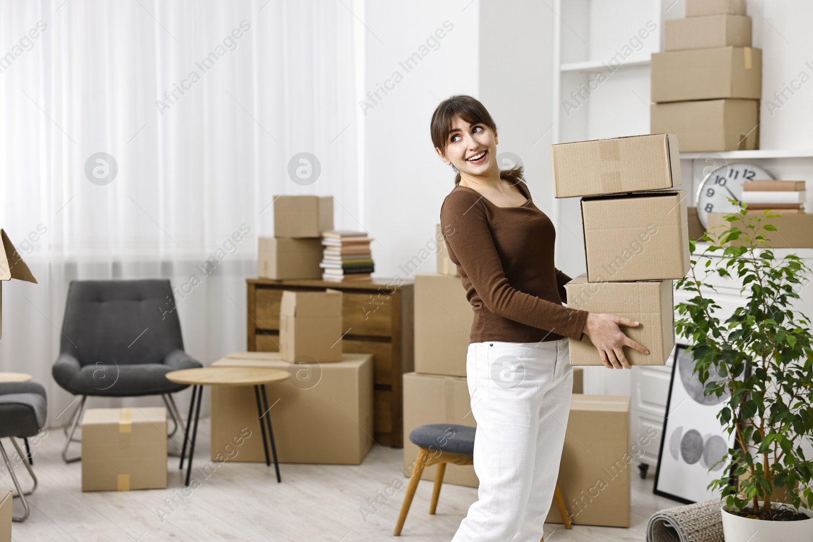 Photo of Moving day. Happy woman with cardboard boxes in her new home