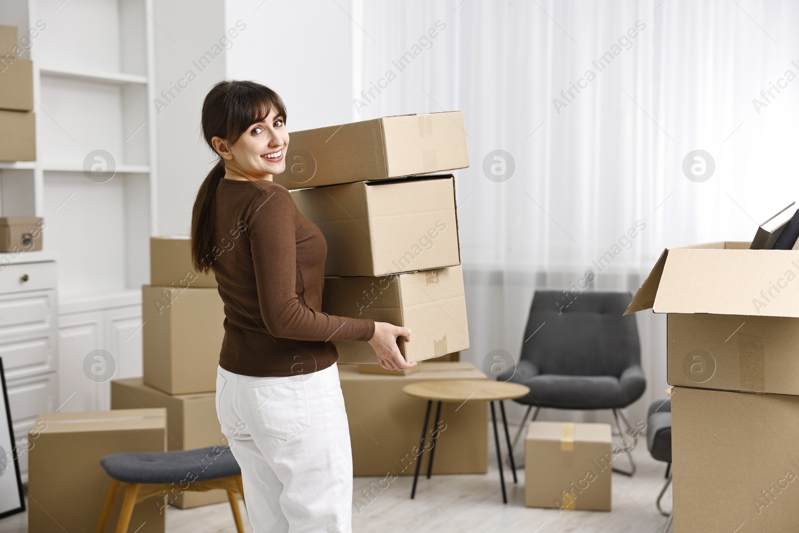 Photo of Moving day. Happy woman with cardboard boxes in her new home