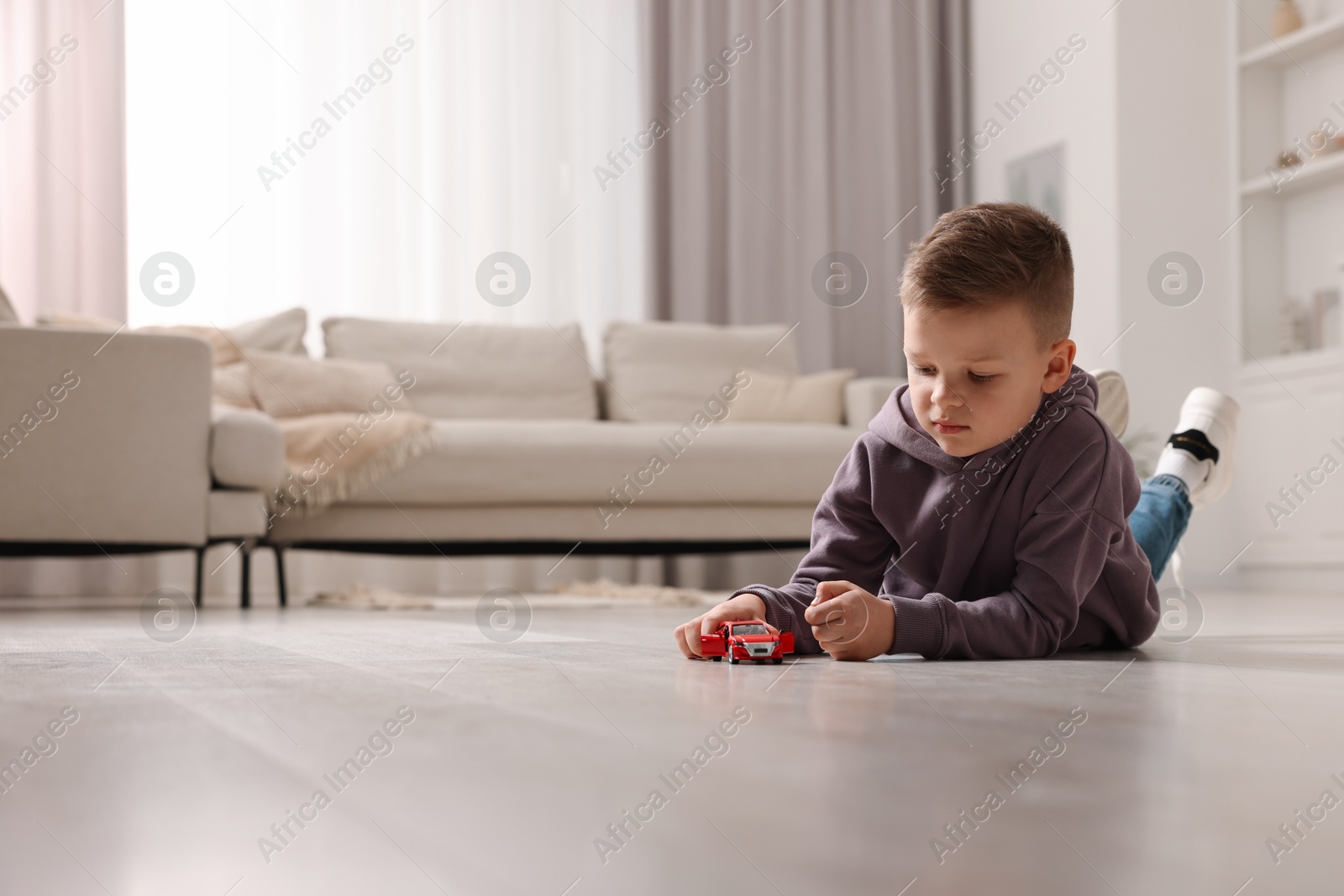 Photo of Little boy playing with toy car at home. Space for text