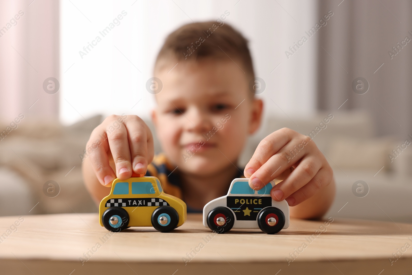 Photo of Little boy playing with toy cars at wooden table indoors, selective focus