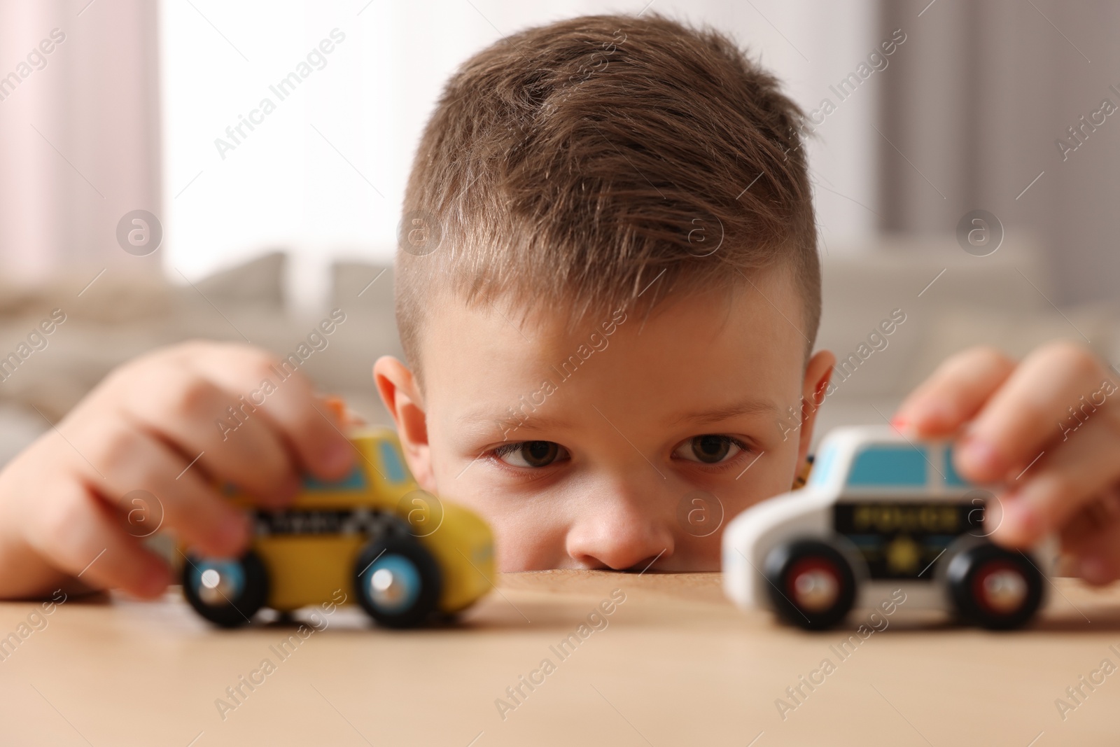 Photo of Little boy playing with toy cars at wooden table indoors