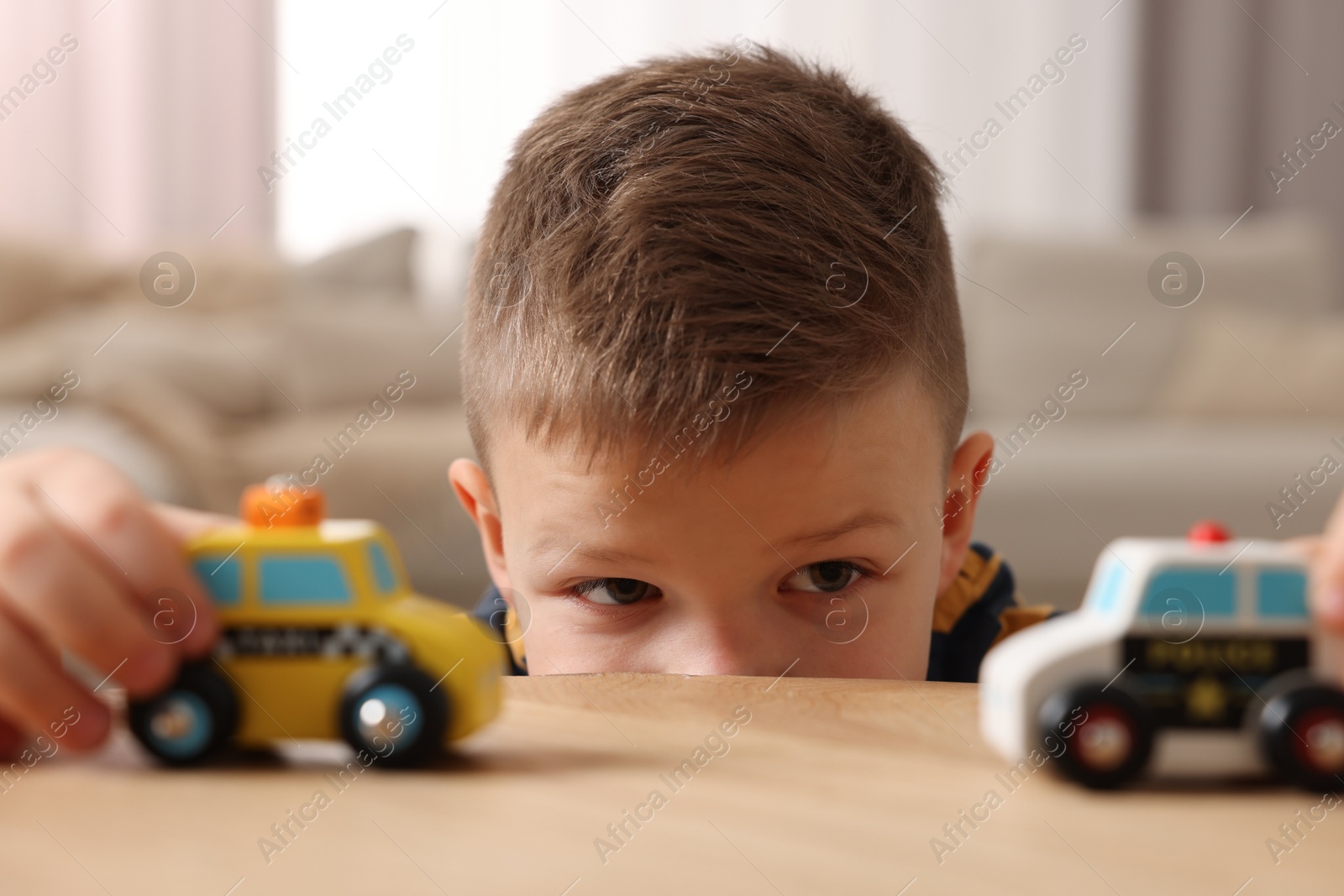 Photo of Little boy playing with toy cars at wooden table indoors