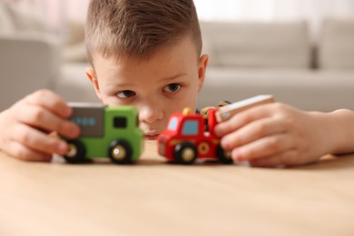 Little boy playing with toy cars at wooden table indoors