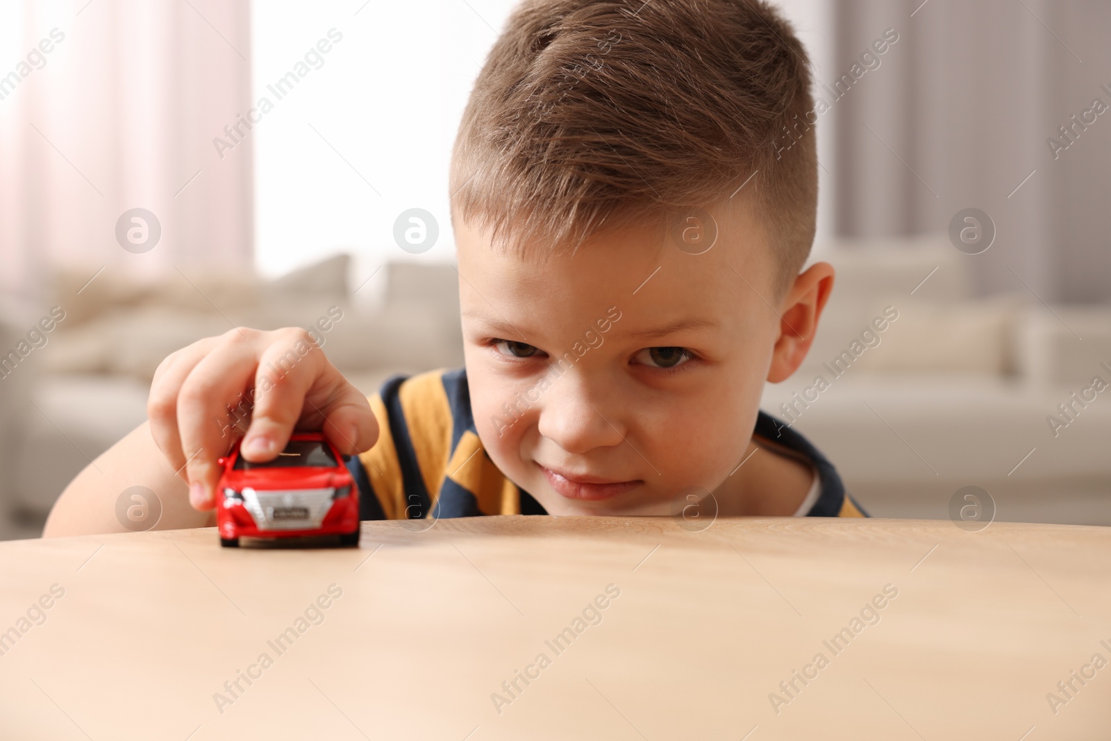 Photo of Little boy playing with toy car at wooden table indoors