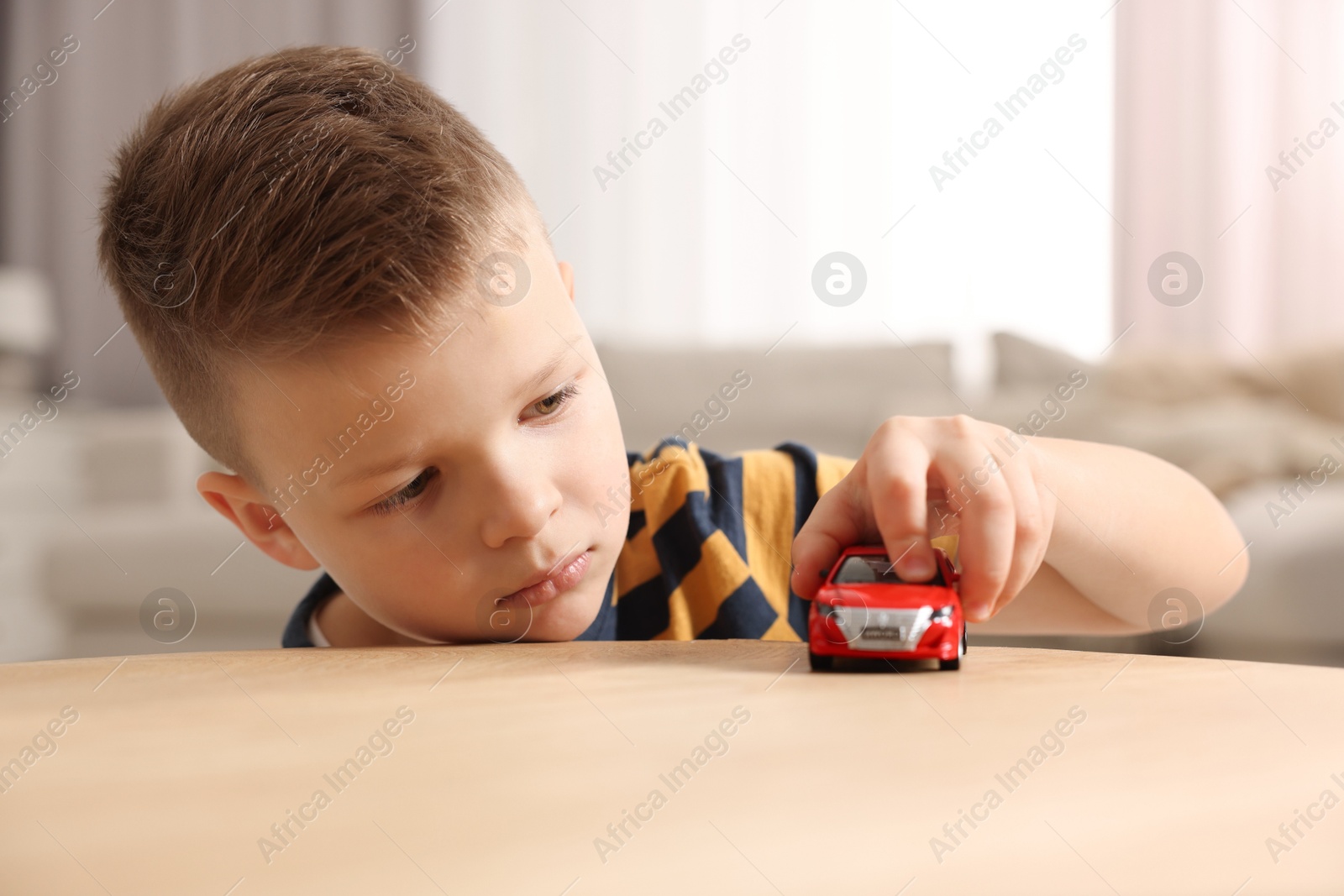 Photo of Little boy playing with toy car at wooden table indoors