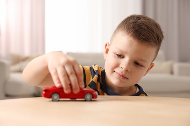 Little boy playing with toy car at wooden table indoors