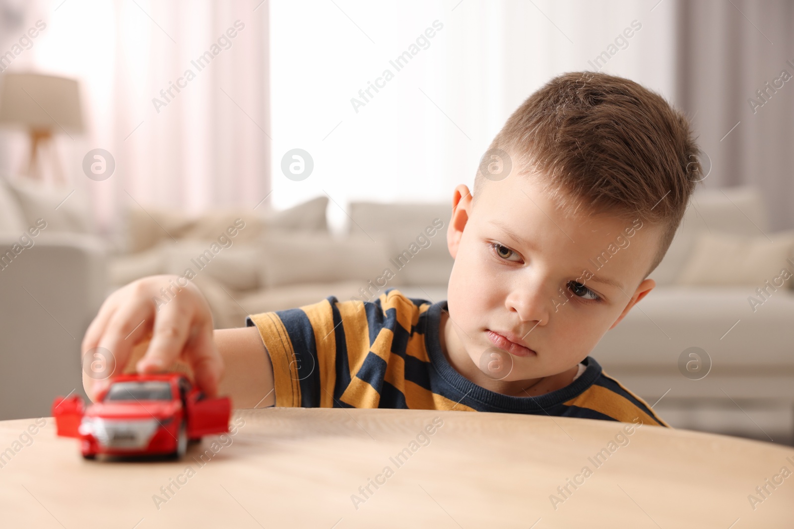 Photo of Little boy playing with toy car at wooden table indoors