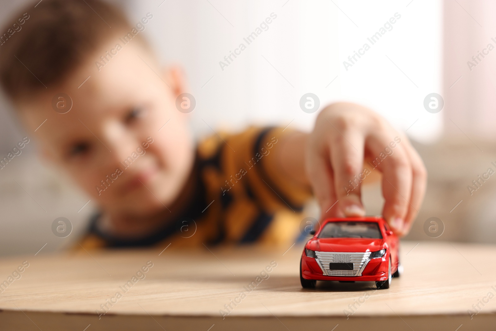 Photo of Little boy playing with toy car at wooden table indoors, selective focus