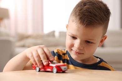 Little boy playing with toy car at wooden table indoors