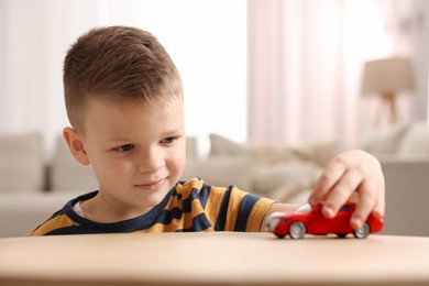 Little boy playing with toy car at wooden table indoors