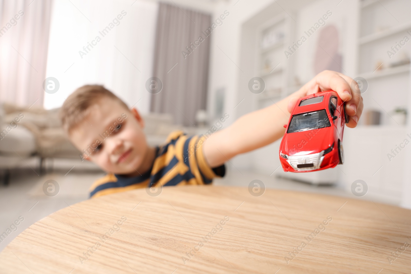 Photo of Little boy playing with toy car at wooden table indoors, selective focus