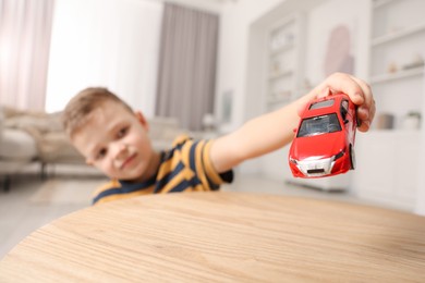 Little boy playing with toy car at wooden table indoors, selective focus