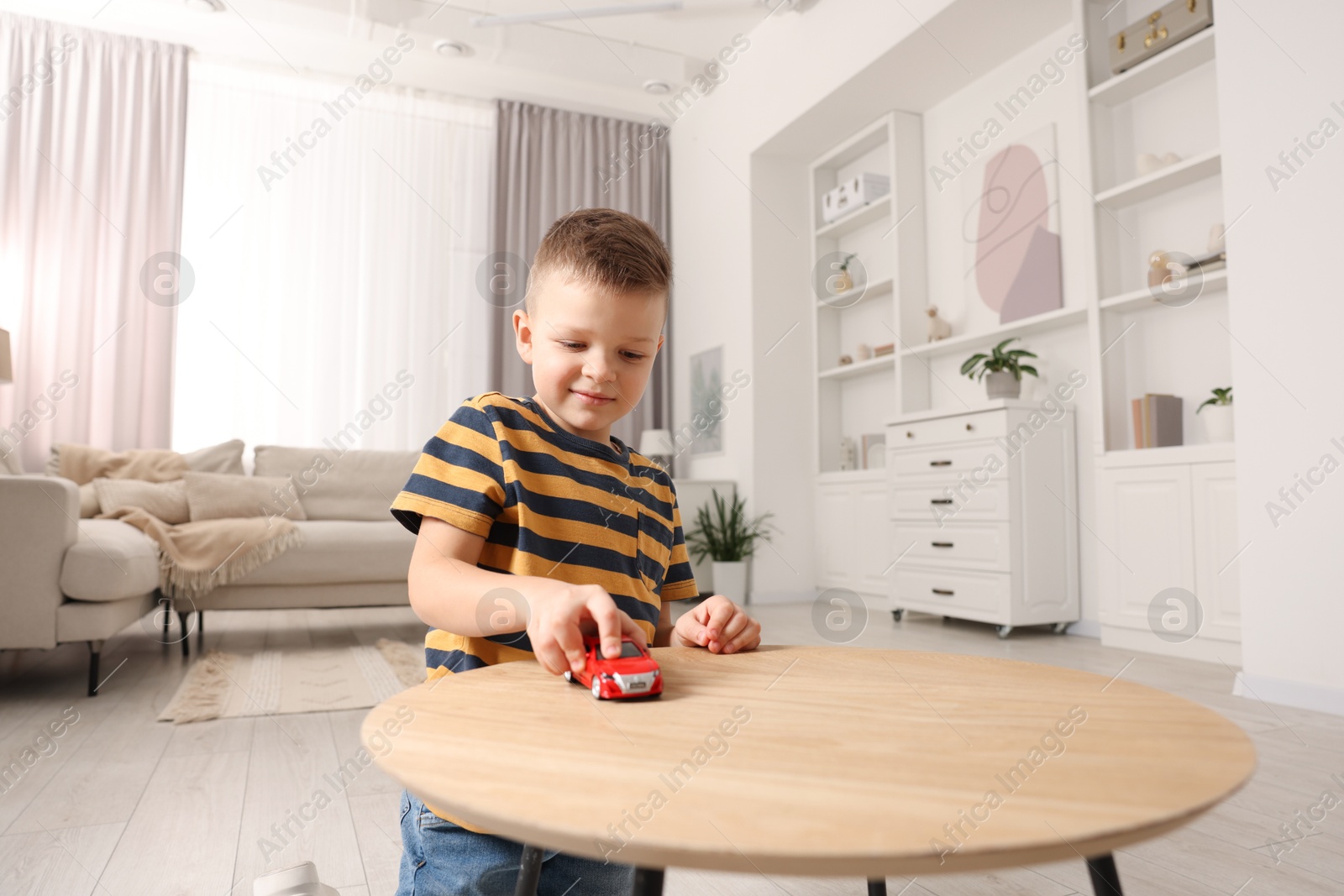 Photo of Little boy playing with toy car at wooden table indoors