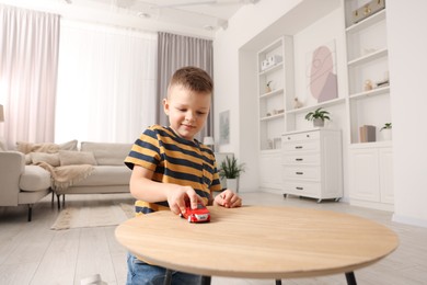 Little boy playing with toy car at wooden table indoors