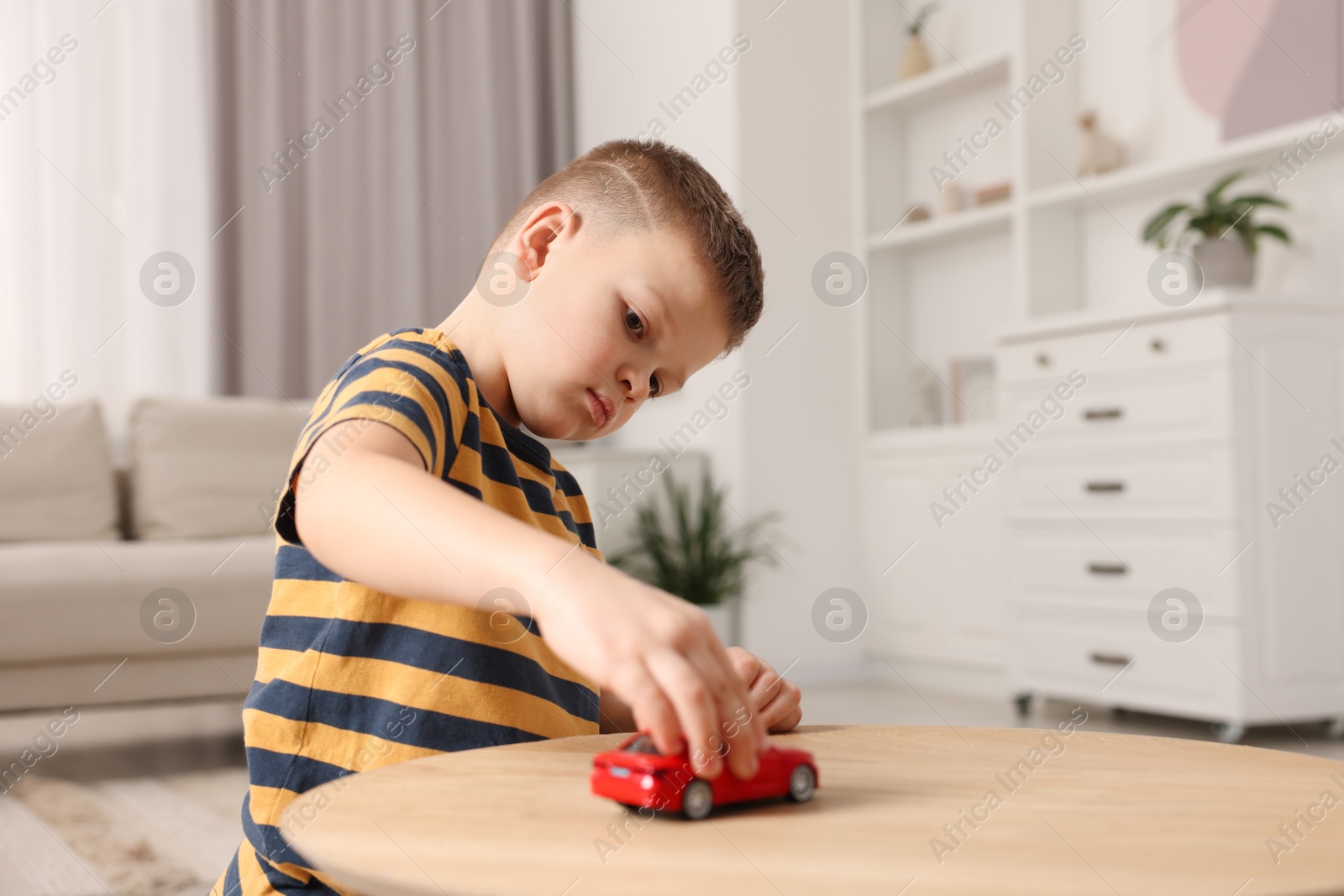 Photo of Little boy playing with toy car at wooden table indoors