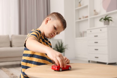 Little boy playing with toy car at wooden table indoors