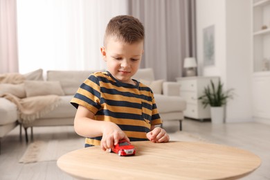 Little boy playing with toy car at wooden table indoors