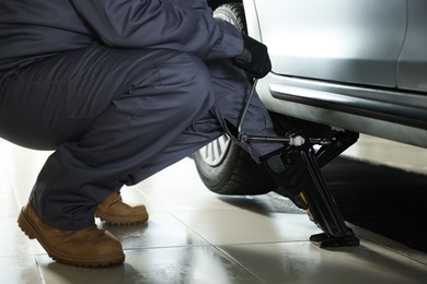 Photo of Auto mechanic lifting car with scissor jack at service station, closeup