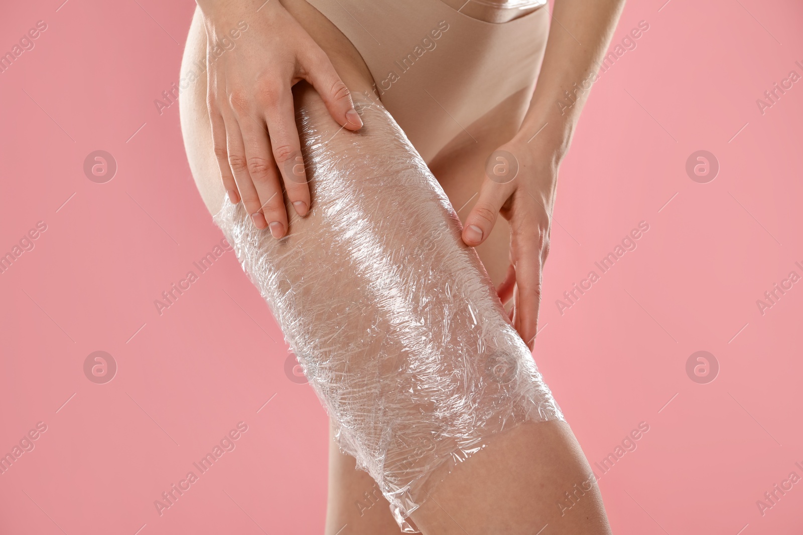 Photo of Woman doing spa body wraps on her leg against pink background, closeup