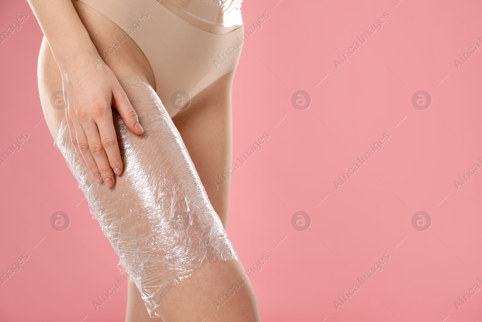 Photo of Woman doing spa body wraps on her leg against pink background, closeup. Space for text