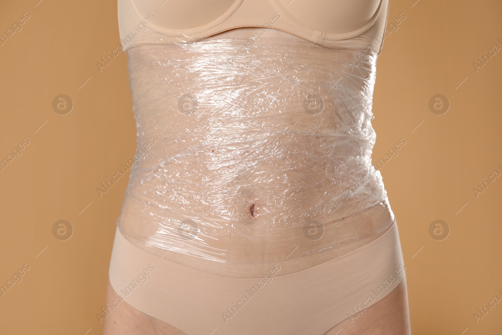 Photo of Woman doing spa body wraps on her belly against beige background, closeup