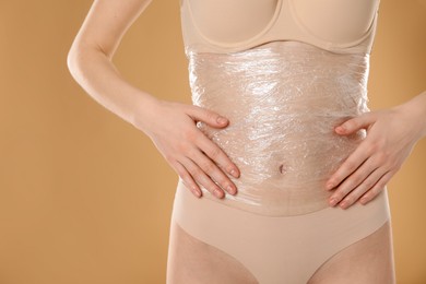 Woman doing spa body wraps on her belly against beige background, closeup