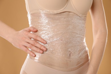 Photo of Woman doing spa body wraps on her belly against beige background, closeup