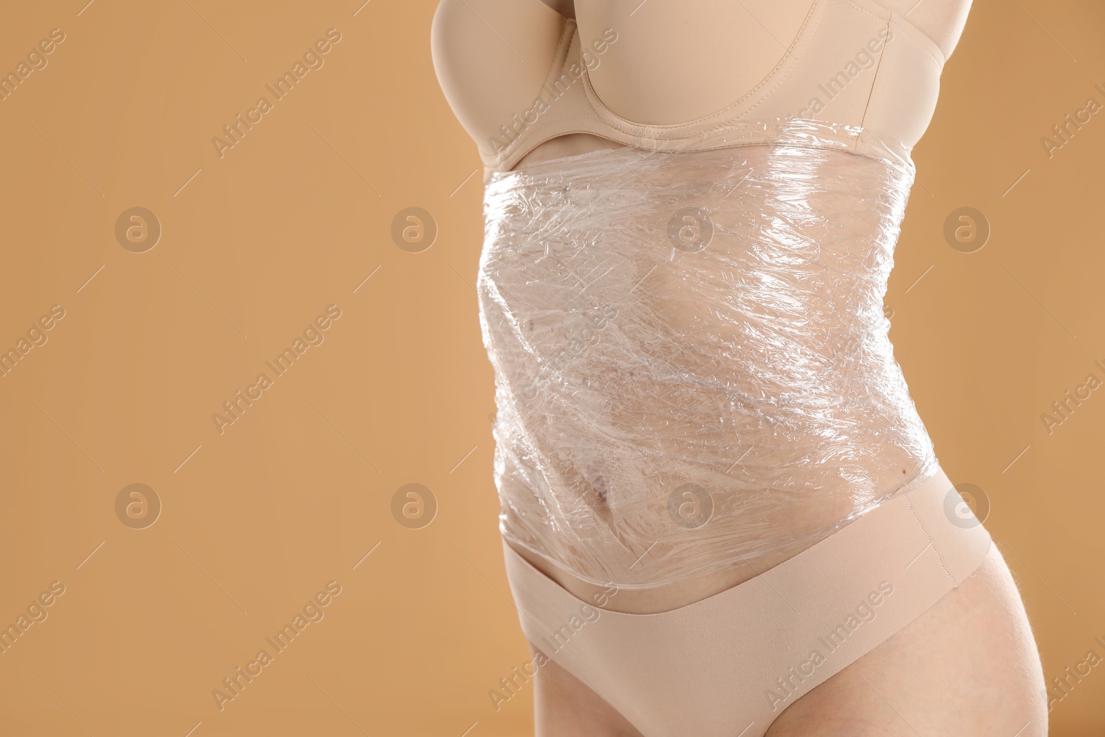 Photo of Woman doing spa body wraps on her belly against beige background, closeup. Space for text