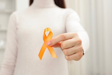 Photo of Multiple Sclerosis awareness. Young woman holding orange ribbon indoors, closeup