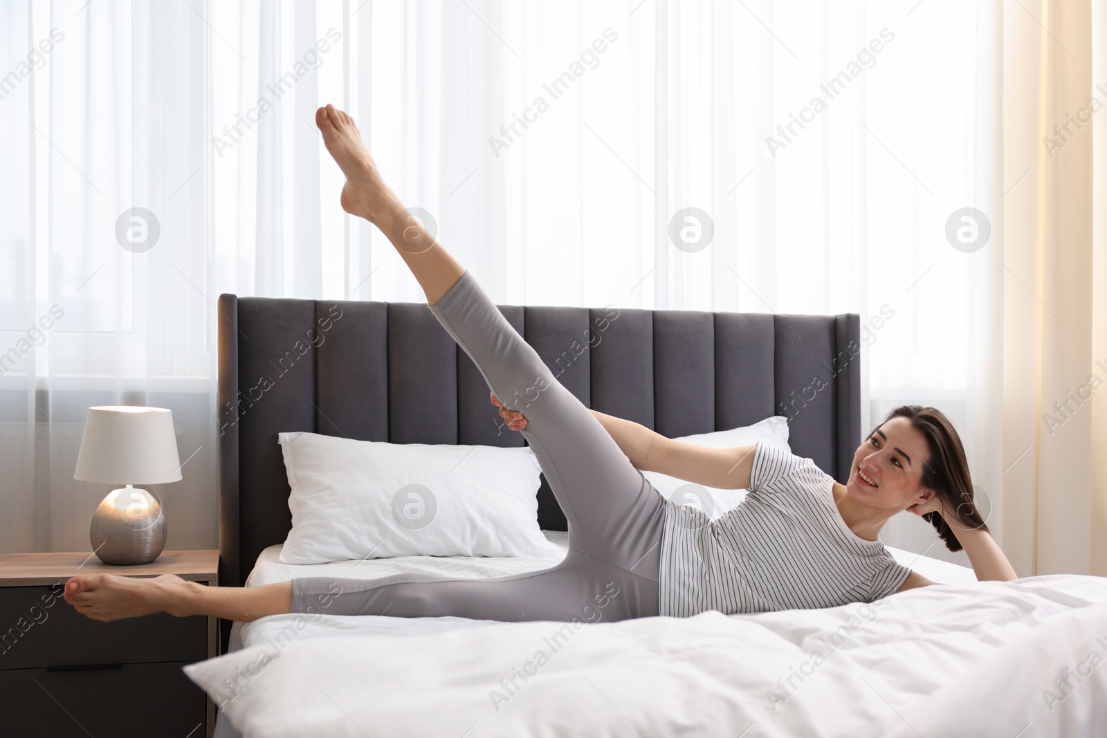 Photo of Young woman exercising on bed at home. Morning routine